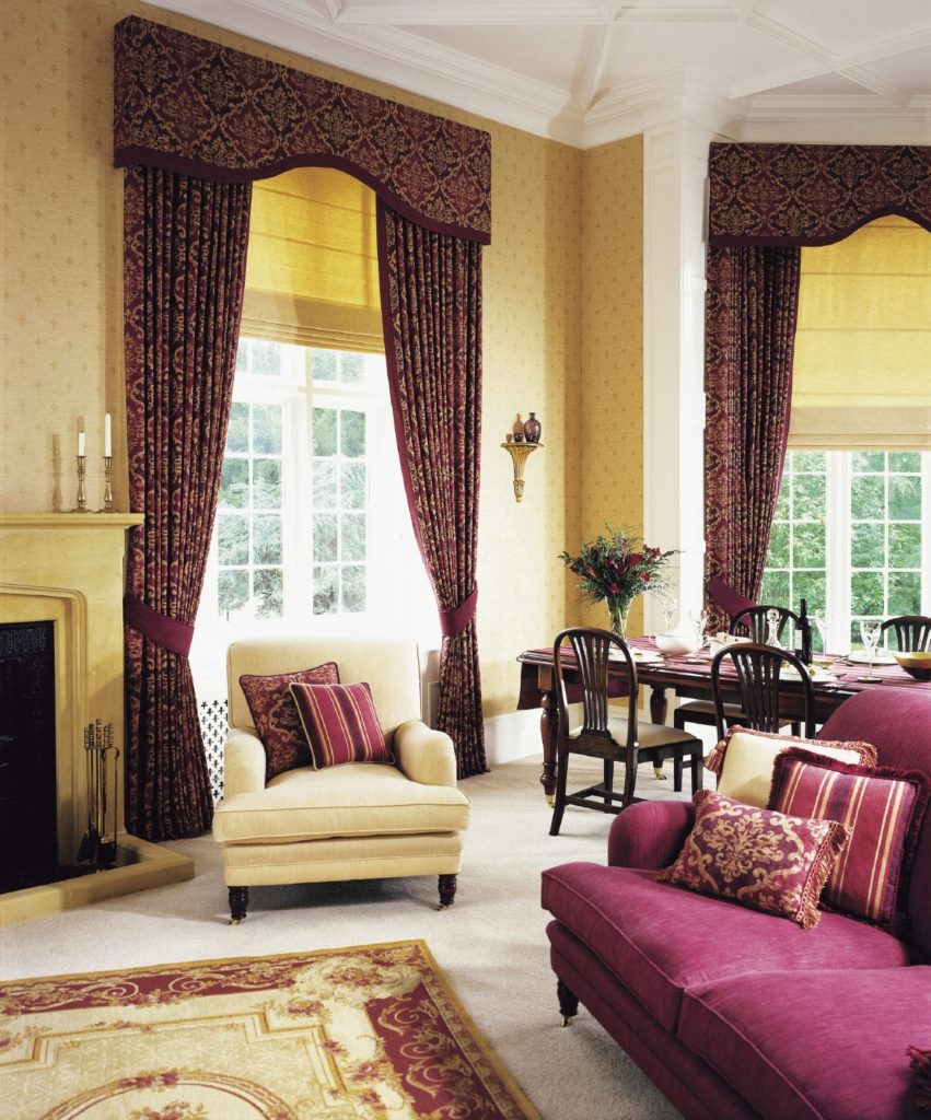 梅花组合沙发与覆盖白色框架窗户的经典图案窗帘相得益彰。这个房间里有一把米色的扶手椅，地毯上铺着一张红色的印花地毯。