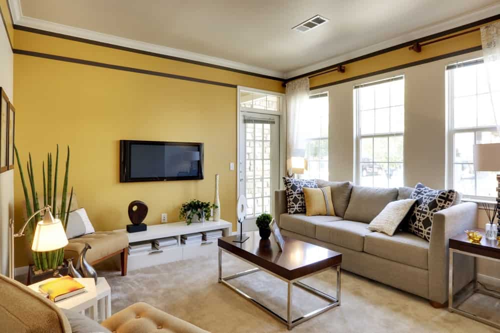 清新的客厅，灰色的组合沙发和米色的簇绒椅子，两侧是白色的模块化边桌。它包括一个金属咖啡桌和挂在光滑的控制台上方的壁挂式电视。
