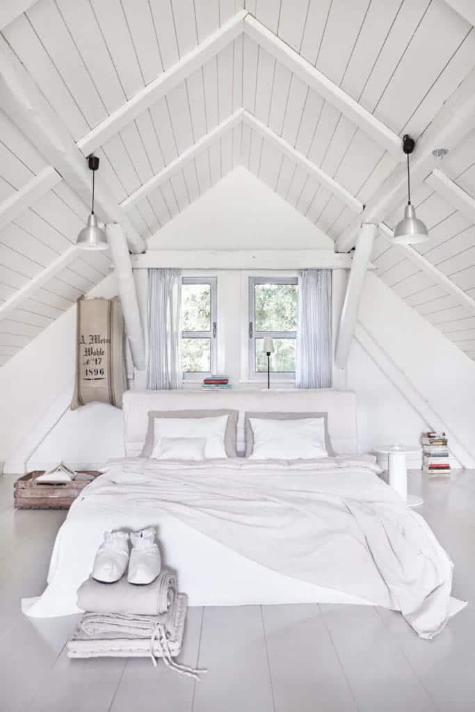 白人的卧室被chrome圆顶吊坠与自然光的玻璃窗都包含在纯粹的窗帘。它有一个舒适的床和一个床头柜在宽木板地板。
