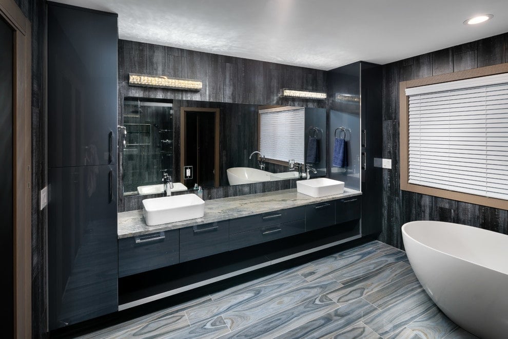 当代主浴室拥有一个独立的浴缸和一个浮动的梳妆台，上面有双容器水槽和米色花岗岩台面。它的两侧是高光泽的橱柜，与木板墙融为一体。