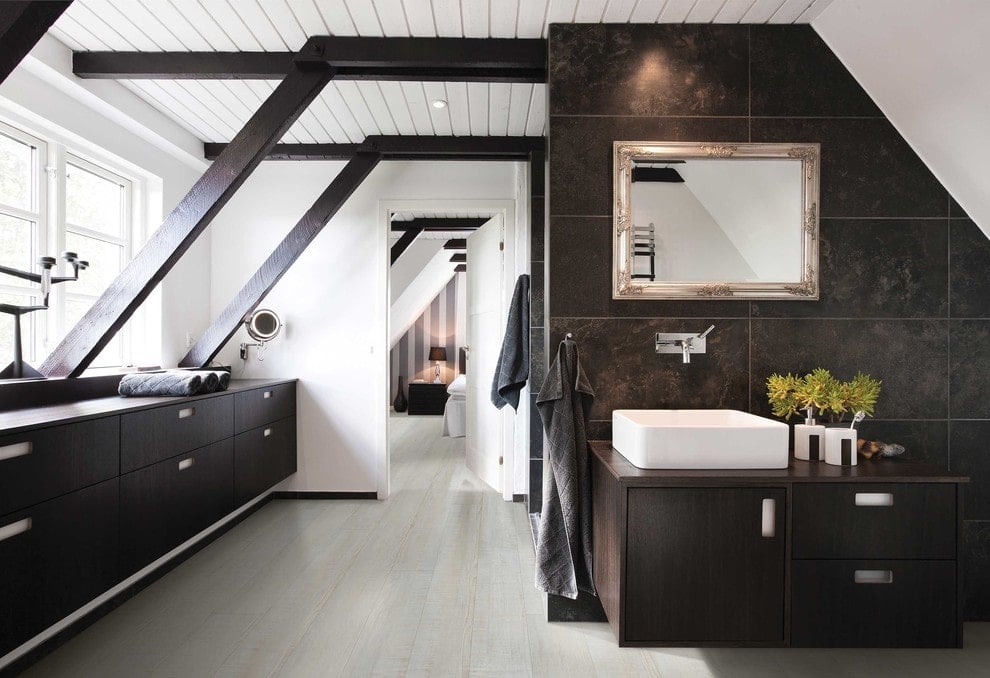 一扇白色的门通往这间主浴室，里面有深色木质储物柜和一个漂浮的梳妆台，梳妆台顶部有一个水槽。它包括一个装在黑色瓷砖墙上的镀铬镜框镜子。