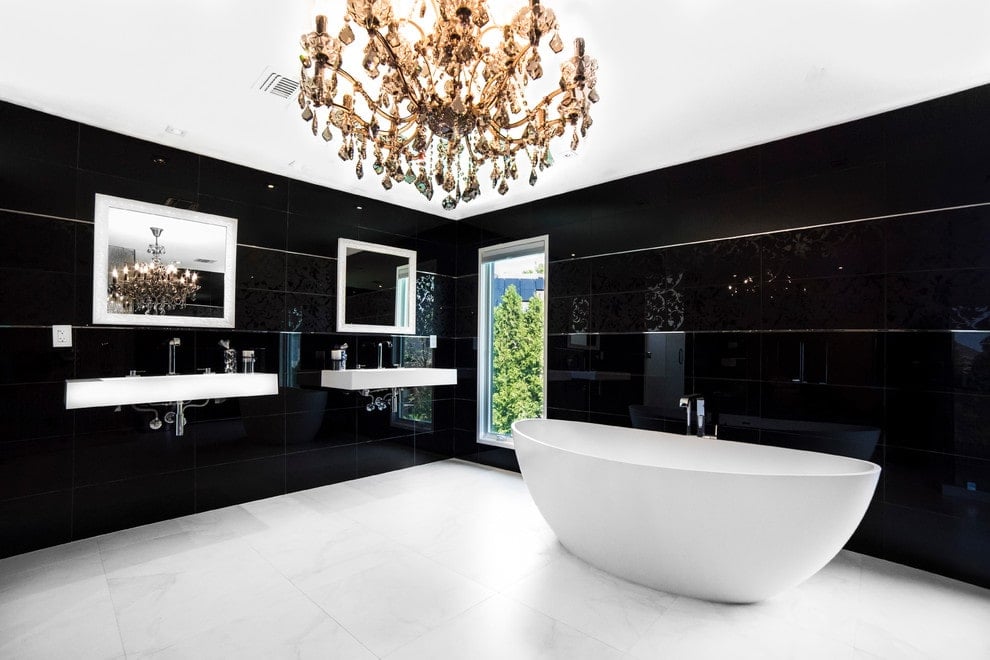 极简主义的主浴室由一个巨大的水晶吊灯和玻璃窗的自然光照亮。它有一个独立的浴缸和壁挂式水槽，配有白色镜框镜子。
