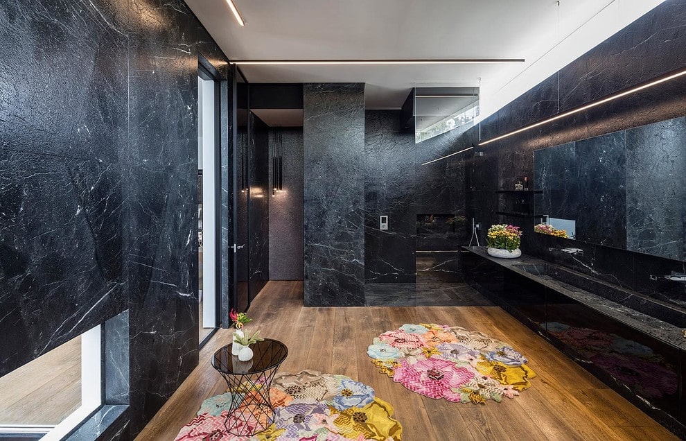 当代风格的主浴室设有步入式淋浴间和水槽，与黑色大理石墙壁融为一体。中间的硬木地板上铺着迷人的碎花地毯。
