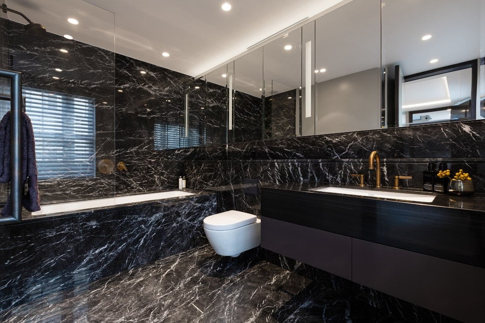 时尚的主浴室设有壁挂式厕所和深泡浴缸，与黑色大理石墙壁和地板相匹配。它包括带镜子的药柜和一个装有黄铜固定装置的浮动洗手台。