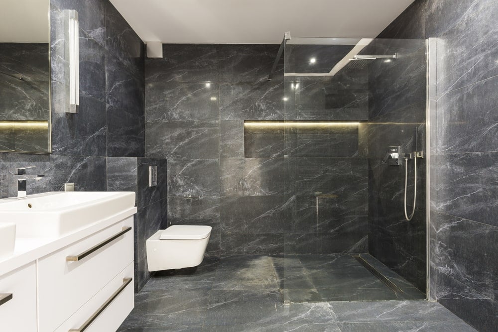 光滑的主浴室设有一个浮动洗手台和一个挂在墙上的卫生间，正对着步入式淋浴间。它有黑色大理石瓷砖地板，墙壁上装有嵌入式书架。
