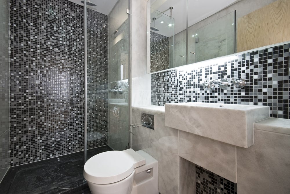 黑色的主浴室带有一个现代化的厕所，镜子药柜下面有一个大理石水槽。它包括一个步入式淋浴，带有令人惊叹的马赛克瓷砖后挡板。