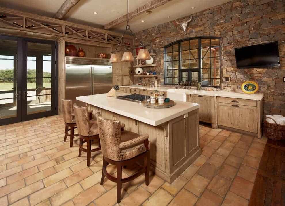 这个厨房拥有内置的酒架，以纵横交错的模式排列，以及与早餐岛搭配的木制柜台椅的木制橱柜。它有砖地板和石头装饰墙，上面有电视和动物头像装饰。