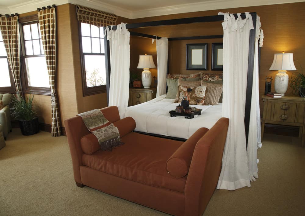 这张照片聚焦在这个主卧室的华丽的床上，棕色的沙发，周围是棕色的墙壁。房间里还铺着地毯。