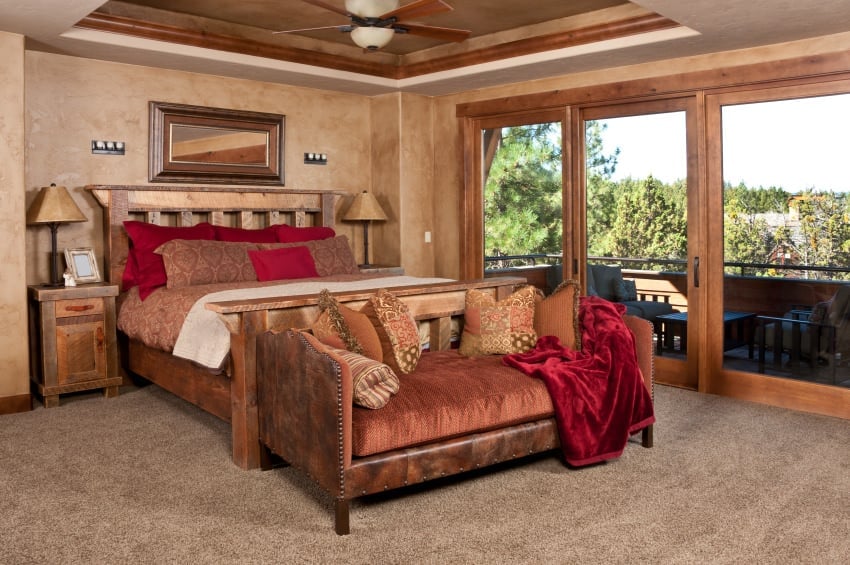 主卧室设有棕色托盘天花板，以及地毯地板和棕色墙壁。房间里有一张华丽的床，有一个木制床架，两边有两盏台灯照明。