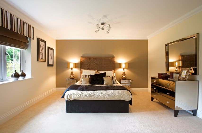 宽敞的主卧室配有华丽的床，两边都有精致的台灯。房间有一面棕色的墙和铺着地毯的地板。