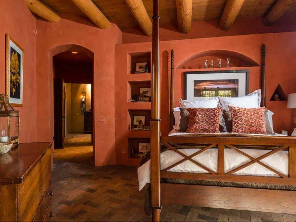 这间主卧室的土褐色墙壁与雪橇床的木质框架以及地板的砖块相得益彰。天花板上裸露的原木横梁和床旁的梳妆台反映了地板的这种色调。