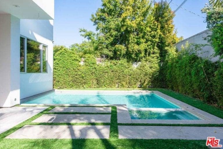 这座住宅有一个小后院，后院有一个被绿色植物和树木包围的游泳池。后院也有维护良好的草坪和一条漂亮的步道。