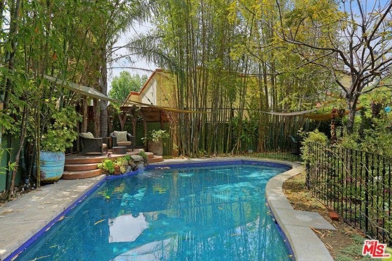 这个游泳池被美丽的成熟树木和绿色植物环绕着。旁边有一个休息区，可以俯瞰美丽的花园。