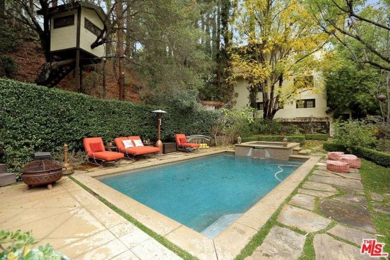 这个住宅的户外区域有一个矩形游泳池，旁边有休息室。这个地区被美丽的植物和树木包围着。
