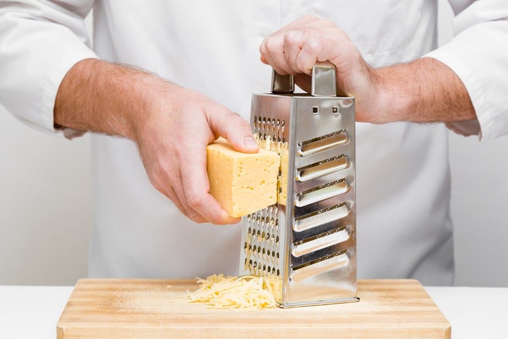 用钢刨丝器把奶酪磨碎。