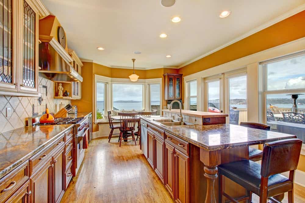 温暖的厨房，木制橱柜和配套的早餐岛搭配黑色软垫椅。它拥有丰富的硬木地板和玻璃镶板窗户，可以俯瞰令人惊叹的室外景色。