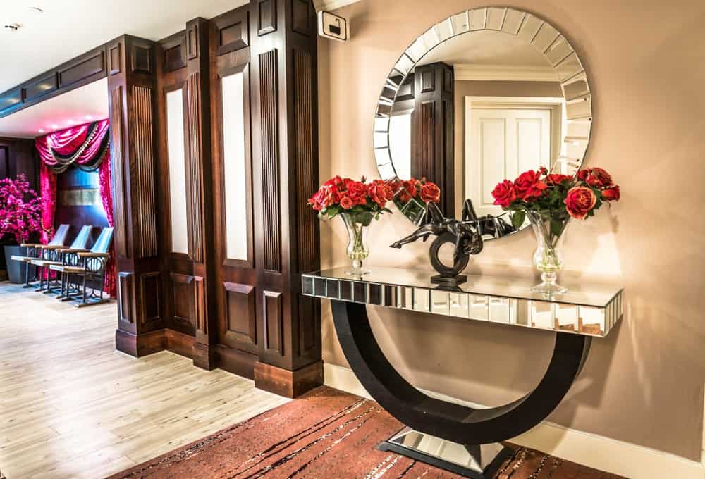 优雅的门厅装饰着一个又大又圆的镜子上面挂一个匹配的桌案上棕色的小地毯。它是覆盖着玻璃花瓶和一个华丽的青铜雕塑。