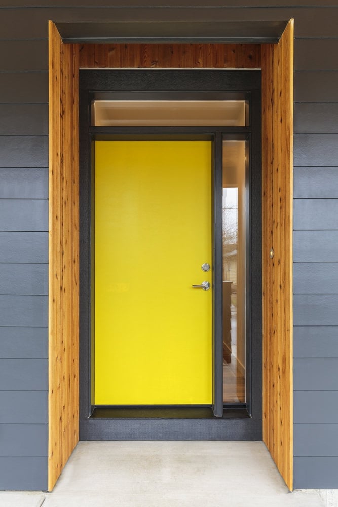一扇黄色的前门，有一面玻璃板和一扇气窗。它充满活力的色彩使它在灰色的墙壁中脱颖而出，尽管它的设计很朴素。