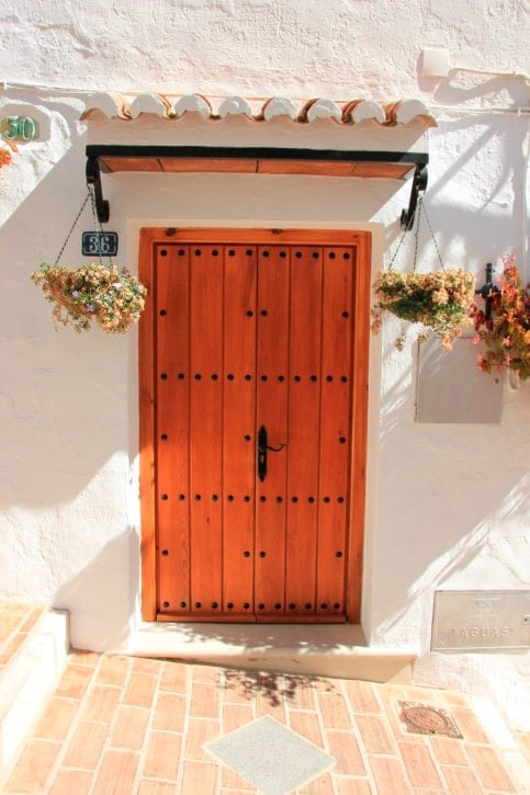 在一个希腊房子的木板条门有铁细节的被固定在屋顶下的可爱的垂悬的植物。