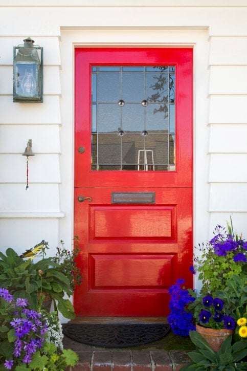 一个经典的红色门，真正脱颖而出。它配有一个迷人的青铜把手和板与玻璃壁灯和安装在白色壁板上的小铃铛相匹配。