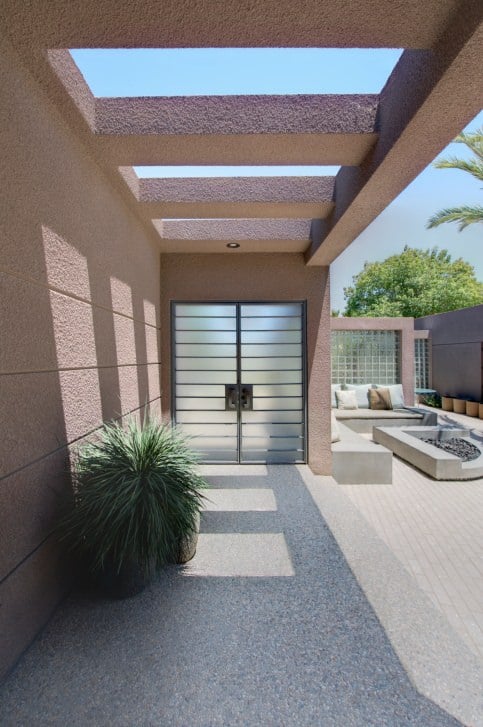 磨砂玻璃门与水平窗格保持了现代住宅的凝聚力，从顶部的混凝土梁一直延续到米色墙壁。绿色的盆栽植物为这个区域增添了柔和的色彩。