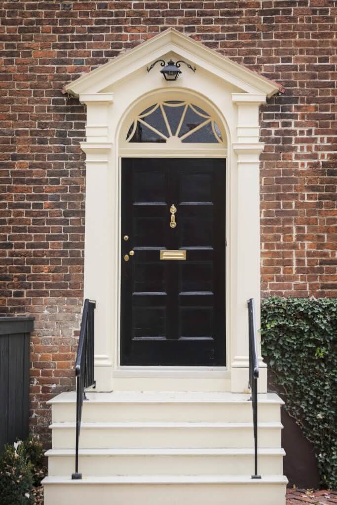 一扇简单的黑色门，由黄铜把手和门板打造而成。它由一个奶油色的门廊和一个匹配的楼梯组成，与锻铁栏杆形成对比。