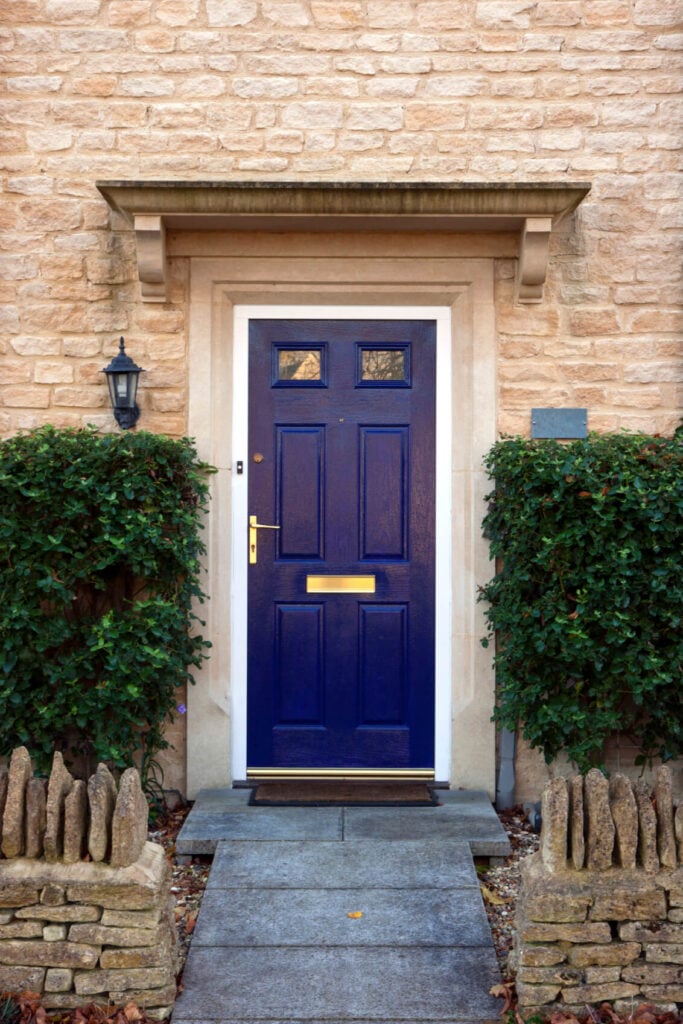 与上面的前门几乎类似，这款带黄铜把手和板块的蓝色门与棕色边界地毯和装在石砖墙上的传统户外扫描配对。