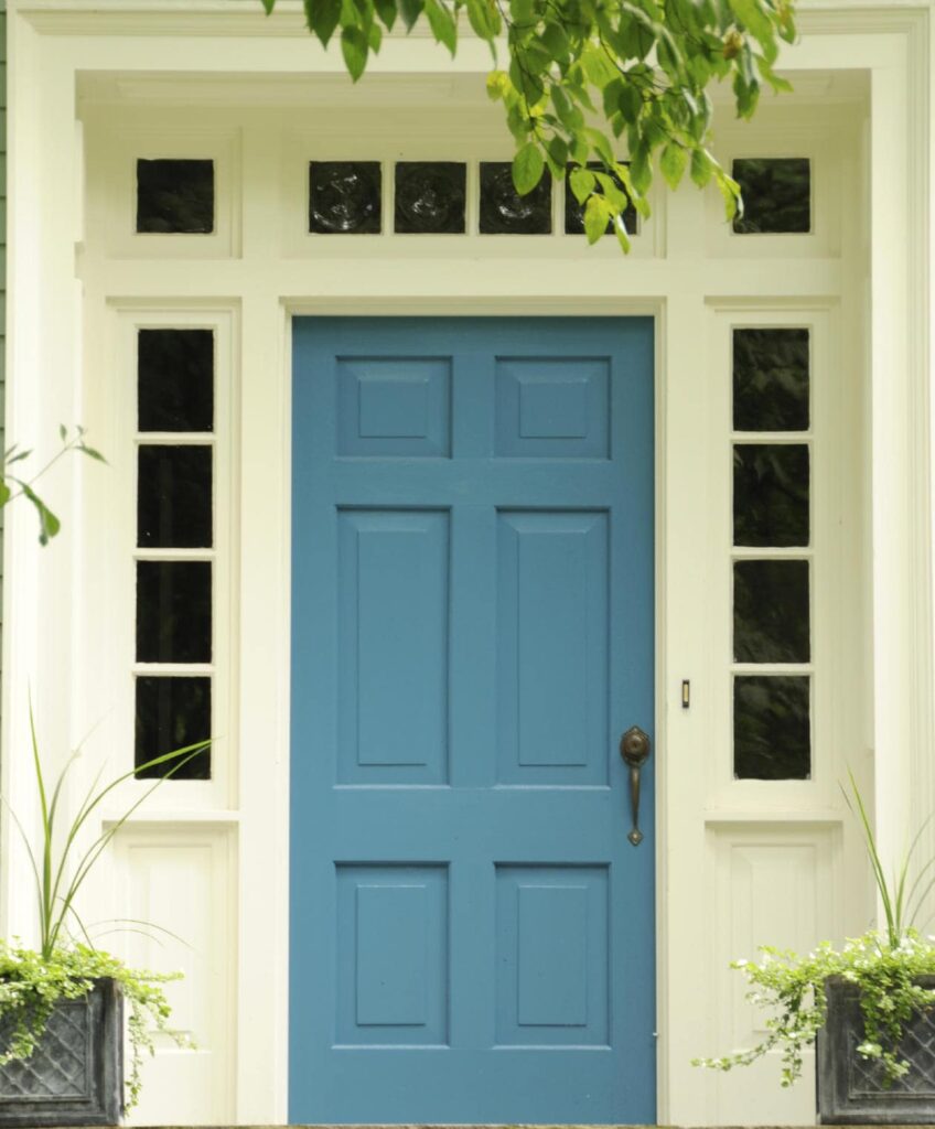 蓝色前门周围有小玻璃板，配有青铜把手。在白色墙壁和绿色植物的映衬下，它显得格外突出。