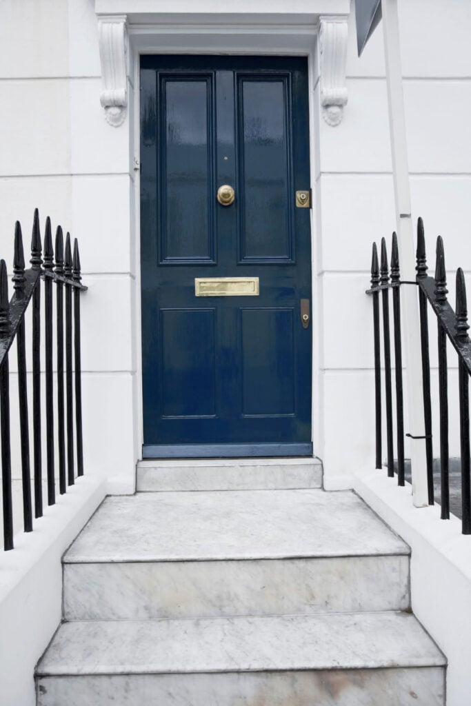 一个不太普通的蓝色前门，表面有光泽。白色的墙壁和铺着铁艺栏杆的楼梯使它显得格外显眼。