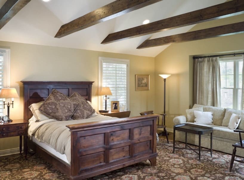 主卧室有一个大的棕色地毯，还有一张乡村框架的高级床和一边的灰色沙发。