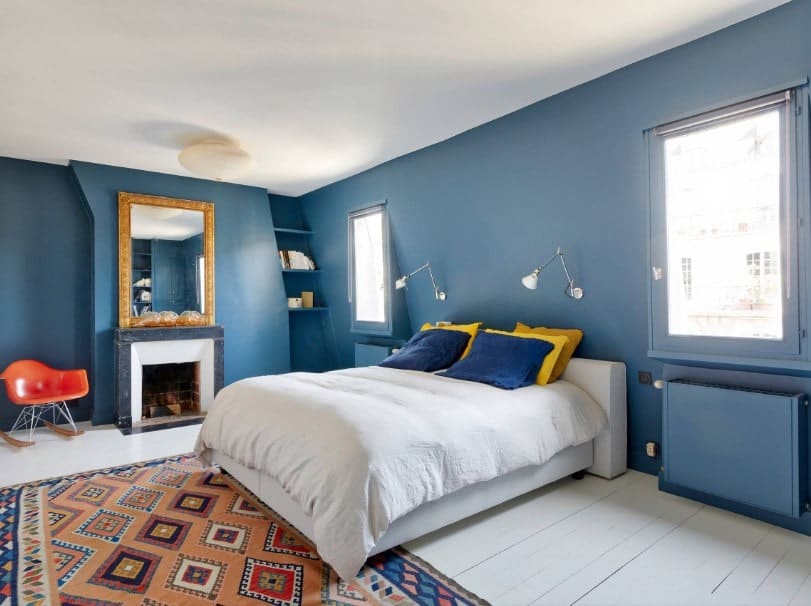 主卧室有蓝色的墙壁和白色的天花板。它的特点是一个舒适的大床，旁边有一个壁炉。