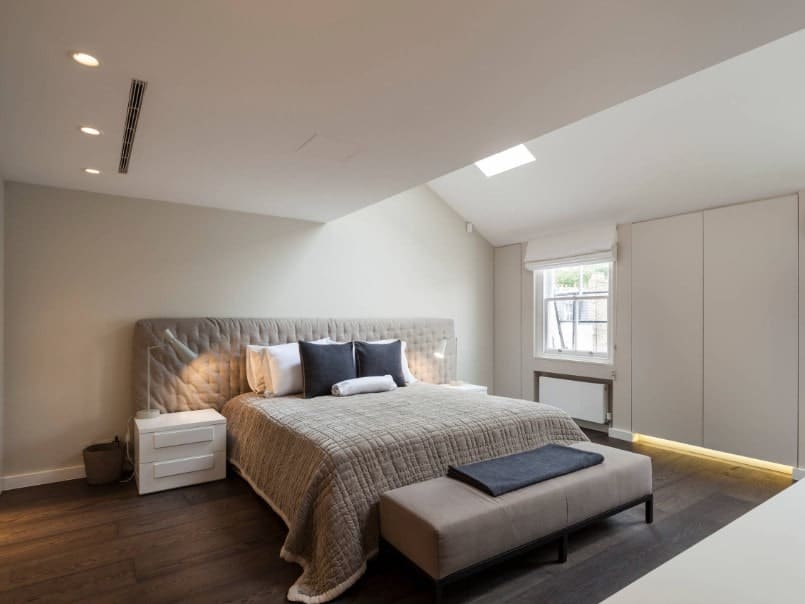 主卧室设有时尚的床设置。房间采用硬木地板、白墙和带天窗的白色棚顶。