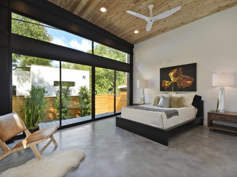 现代化的主卧室，有一张舒适的床和一边的椅子。房间的特色是灰色地板和木棚天花板。