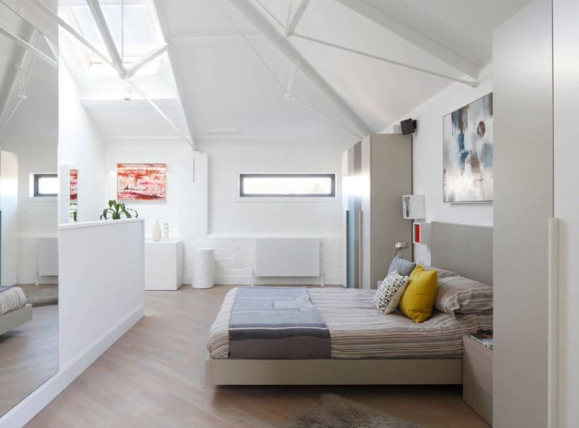 一间宽敞的主卧，有硬木地板、白墙和带天窗的白色棚顶。房间里有一张舒适的大床。