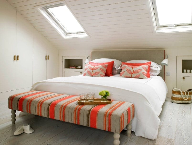 一个集中镜头在这个主卧室的舒适的床与橙色的口音。房间设有带天窗的棚顶。
