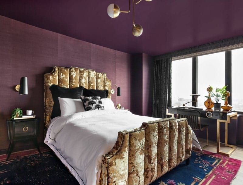 近距离观察这个主卧室的时尚迷彩风格的床架，舒适的床设置由两侧的两盏黑色壁灯照亮。房间的特点是紫色的天花板和紫色的墙壁。