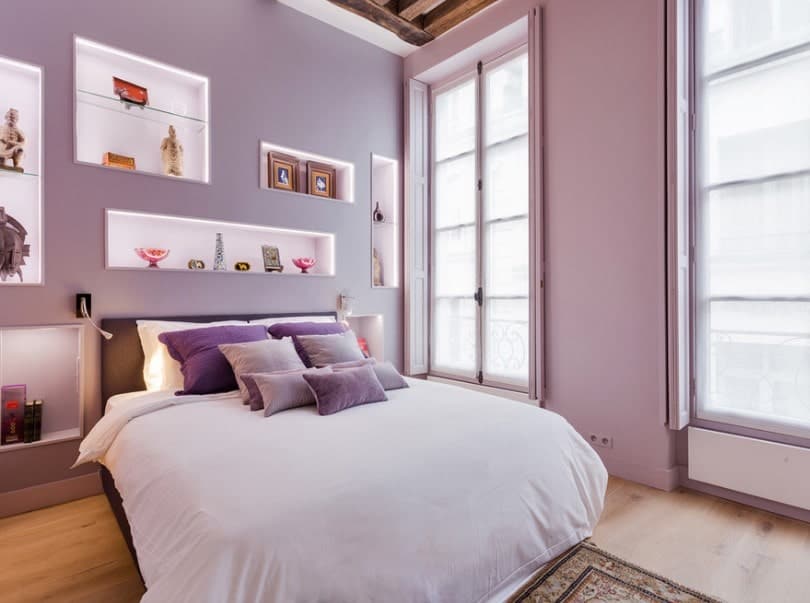 这间主卧室以紫色墙壁为特色，带有多个墙壁装饰，以及硬木地板和带横梁的高天花板。