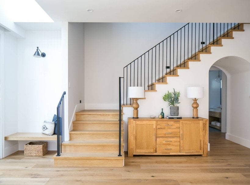 一个聚焦的镜头在这个家庭入口的四分之一转弯楼梯上，有硬木台阶和铁栏杆，被家庭的白墙包围着。