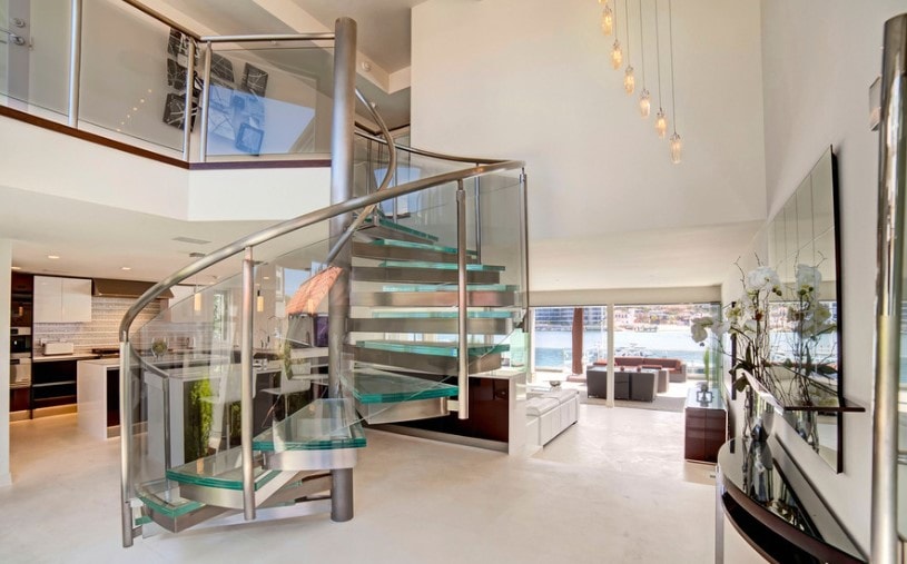 这个现代住宅的时尚楼梯拥有玻璃台阶和玻璃栏杆，由悬挂在高高的天花板上的迷人的天花板灯照亮。