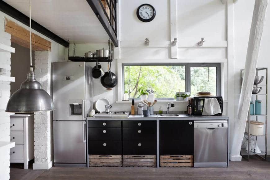白色厨房对比的黑色的盆架,上面挂着不锈钢橱柜和冰箱。它有天然实木地板和一个邀请自然光的玻璃窗。