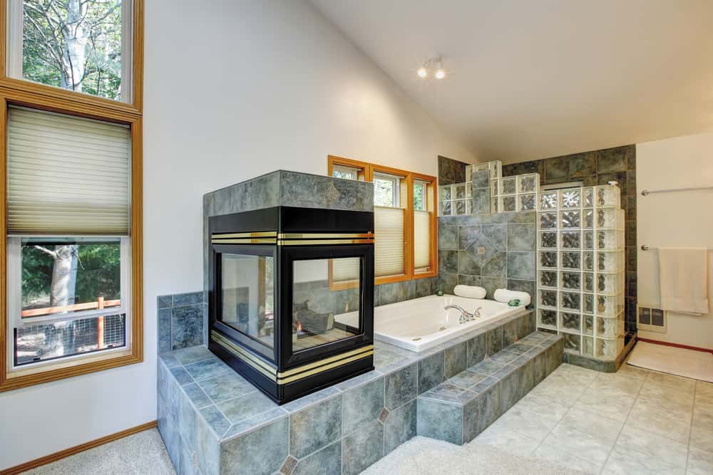 三面壁炉点缀着金色装饰，为主浴室增添了温暖，深浴缸和木框窗户让自然光进入。
