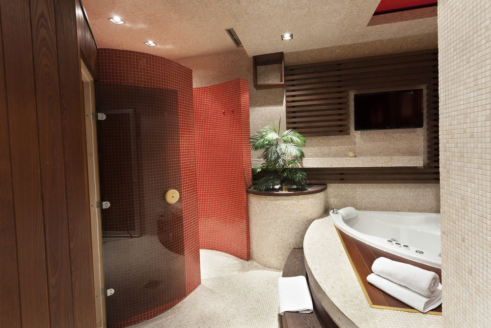 豪华主浴室，设有落体式浴缸和步入式淋浴间，浴室内的弧形墙壁覆盖着红色马赛克瓷砖。中间有一个棕榈植物，在房间里创造了一种热带的感觉。