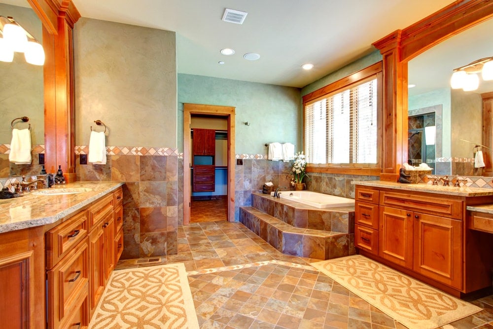 温暖的主浴室有一个深浴缸和木制梳妆台面对彼此。它搭配有图案的地毯，铺在石灰岩地板上。