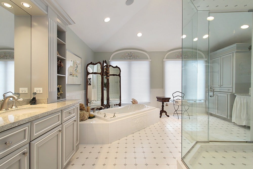 宽敞的主浴室，设有步入式淋浴间和一个浸泡浴缸，旁边是洗手台和花岗岩台面。它包括一个三面板的镜子和安装在拱形天花板上的嵌入式灯。