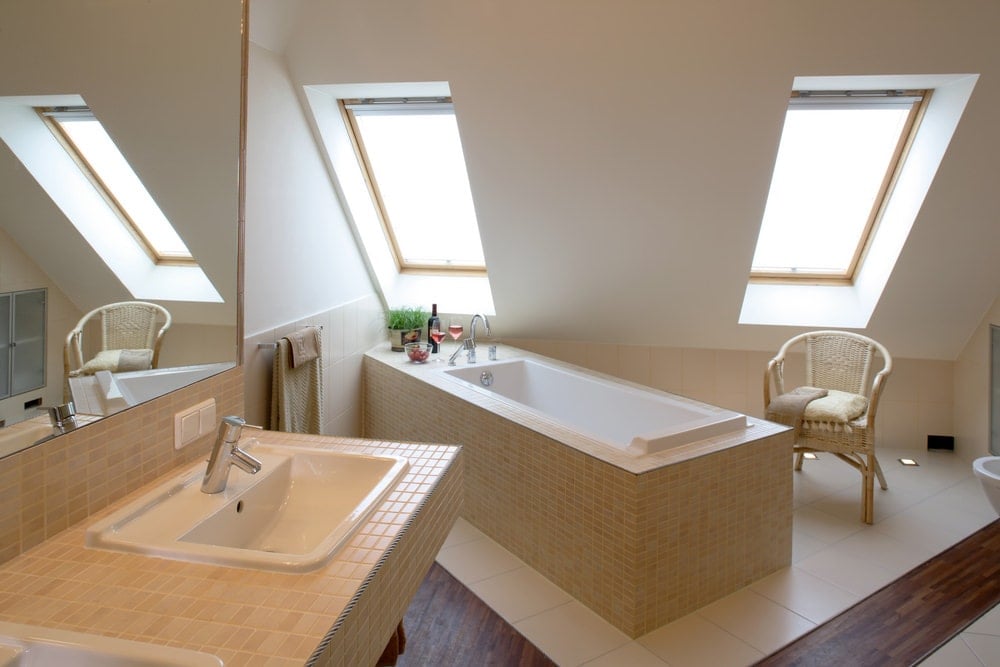 木制圆形椅子面向米色马赛克瓷砖的角落浴缸。这间主要浴室配有瓷砖地板和带天窗窗户的拱形墙。