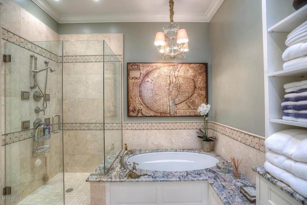 一个镀铬吊灯照亮了主浴室，提供了步入式淋浴和内置长凳的落体式浴缸。顶部灰色的墙上挂着一件有趣的艺术品。
