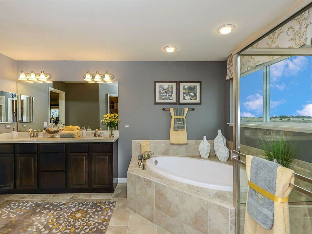 花墙艺术补充灰色印花地毯，铺在米色瓷砖地板延伸到浴缸周围。主浴室展示了一个深色木质梳妆台和玻璃窗，可以俯瞰广阔的视野。