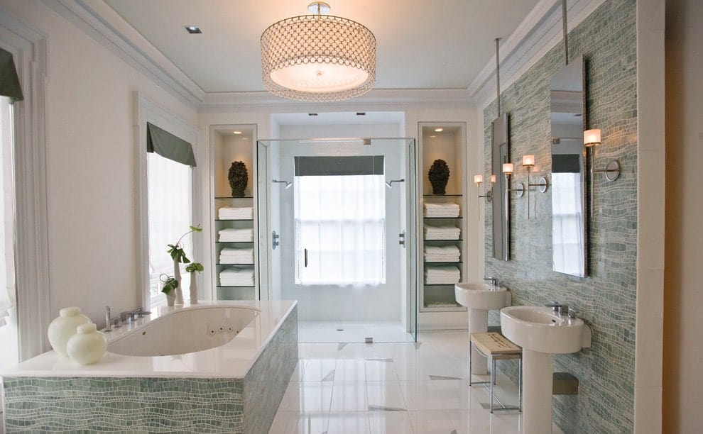 绿色瓷砖强调墙与浴缸周围的玻璃窗搭配白色透明窗帘。这间主浴室设有一对基座式水槽和一个步入式淋浴间，他和她的淋浴头两侧设有嵌入式搁板。