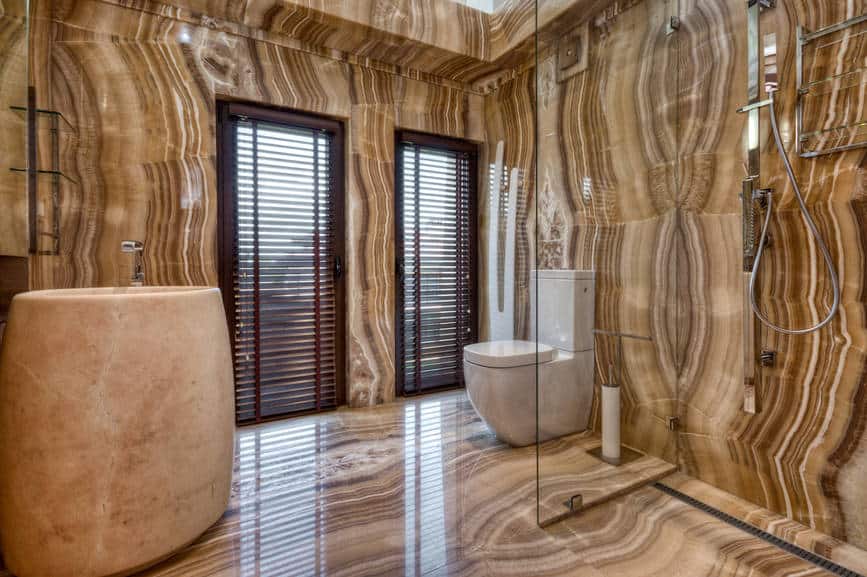 优雅的主浴室，奇妙的棕色瓷砖墙壁和地板，具有凝聚力的外观。它有一个淋浴和厕所区，由无框玻璃隔开，还有一个装有铬水龙头的大型底座水槽。