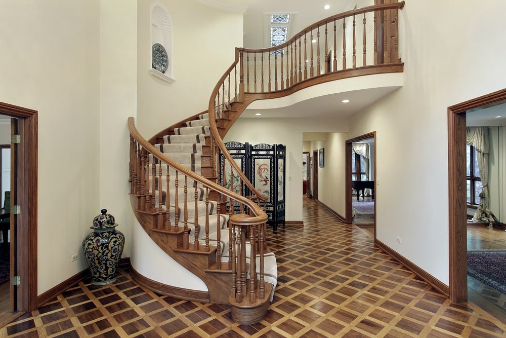 这个门厅的旋转楼梯有木栏杆和木台阶，大部分都覆盖着米黄色的地毯。这个木制楼梯与硬木地板很好地搭配，有一个格子图案，与简单的白色墙壁形成对比。